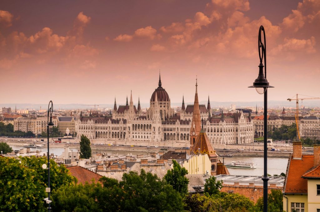 Panoramic view of the Hungarian Parliament Building in Budapest across the Danube at sunset, with city rooftops in the foreground