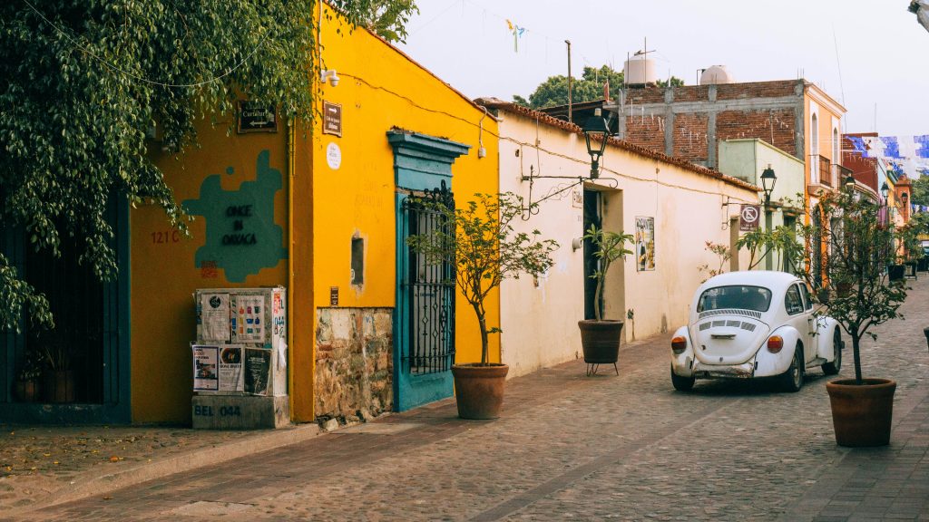 Colorful street in Oaxaca, Mexico with a vintage white Volkswagen Beetle and colonial buildings.