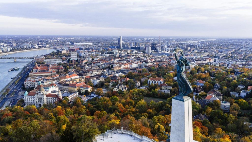 Panoramic city view with statue and river in autumn.