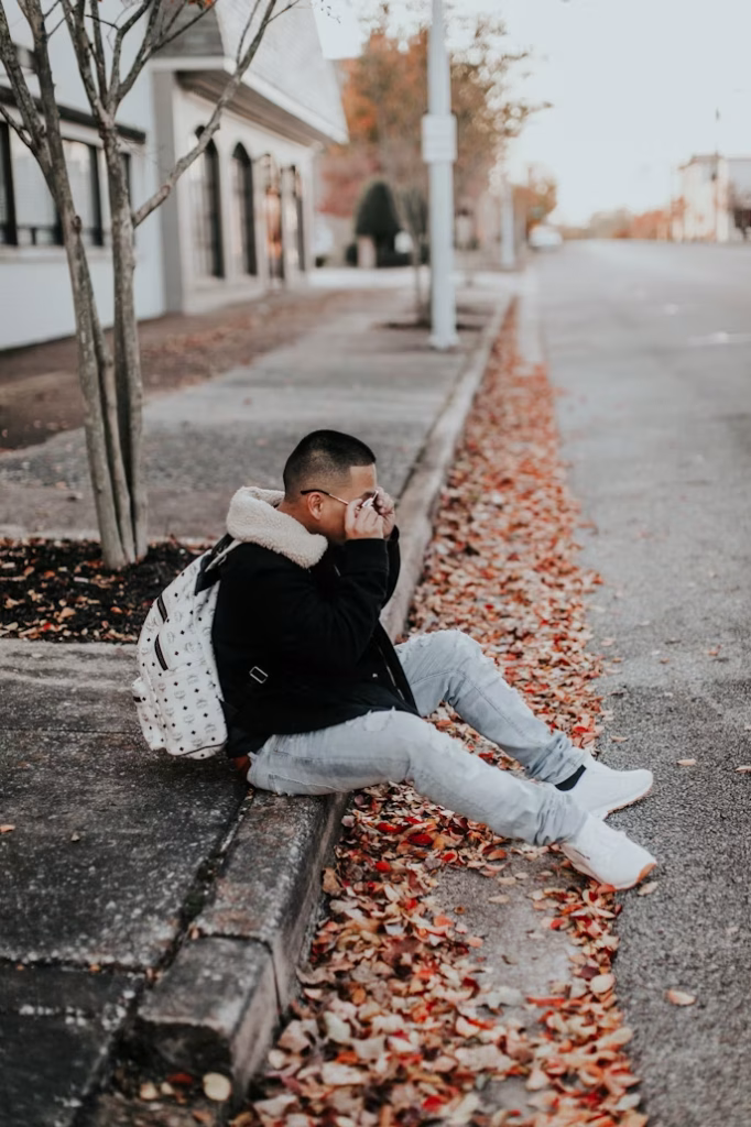 Person sitting on sidewalk with autumn leaves